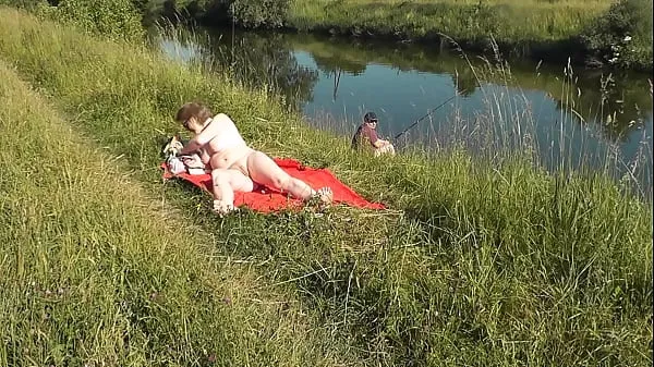 Stort MILF sexy Frina on river bank undressed and sunbathes naked. Random man fisherman watching for her, and in the end decided to join naked woman. Wild beach. Nudist beach. Public nudity. Public exposure. Naked in public varmt rör